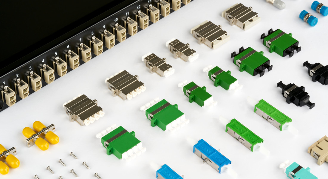 Verschiedene Glasfaser-Kupplungen vor einem Patchpanel mit nummerierten Ports.