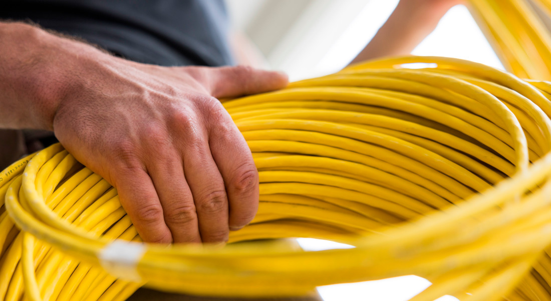 Nærbillede af en hånd med en gul kabeltromle - professionel netværkskabling til IT-infrastrukturer