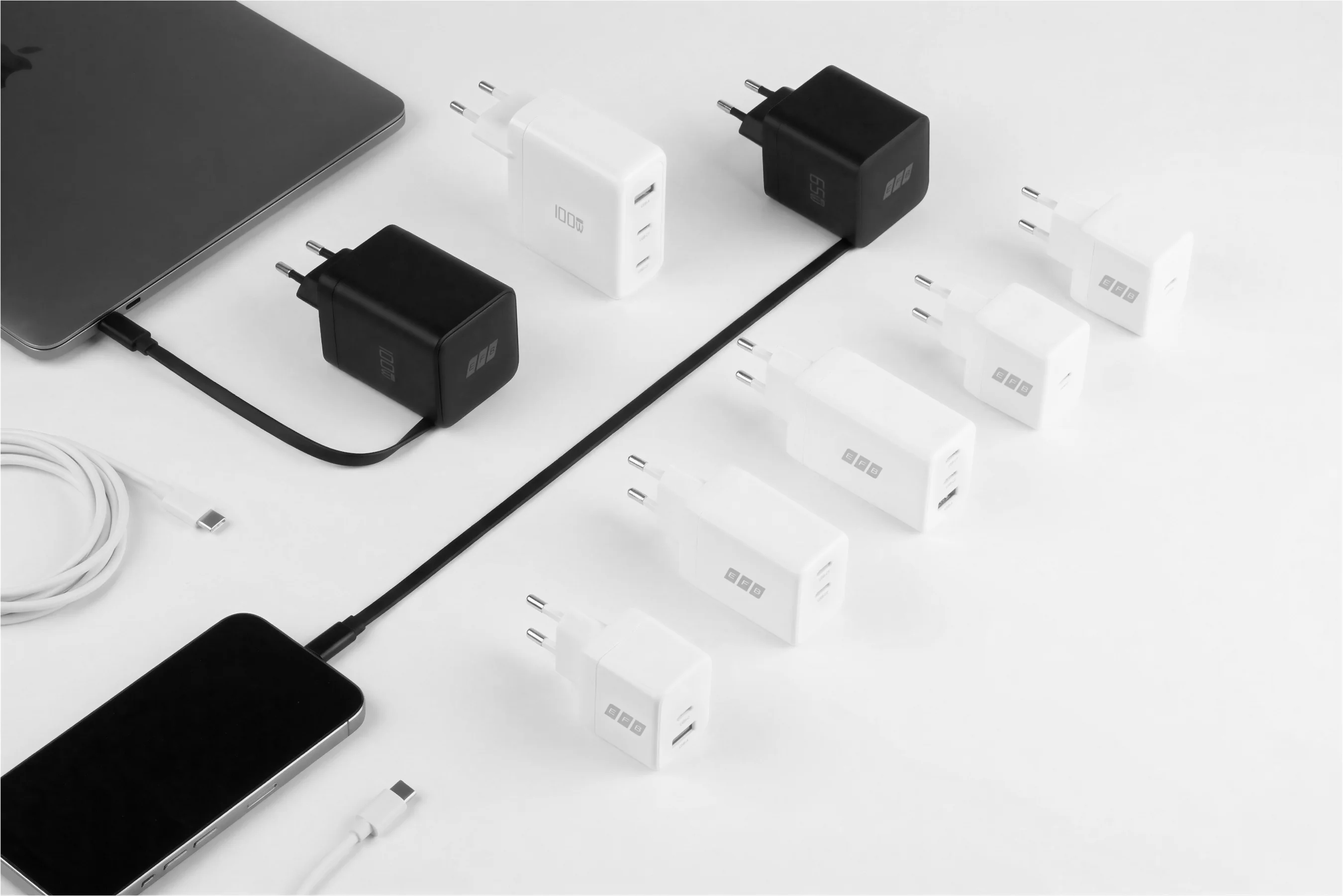 Several USB-C chargers in black and white (65W and 100W) on a white background, alongside a smartphone, tablet, and USB-C charging cable